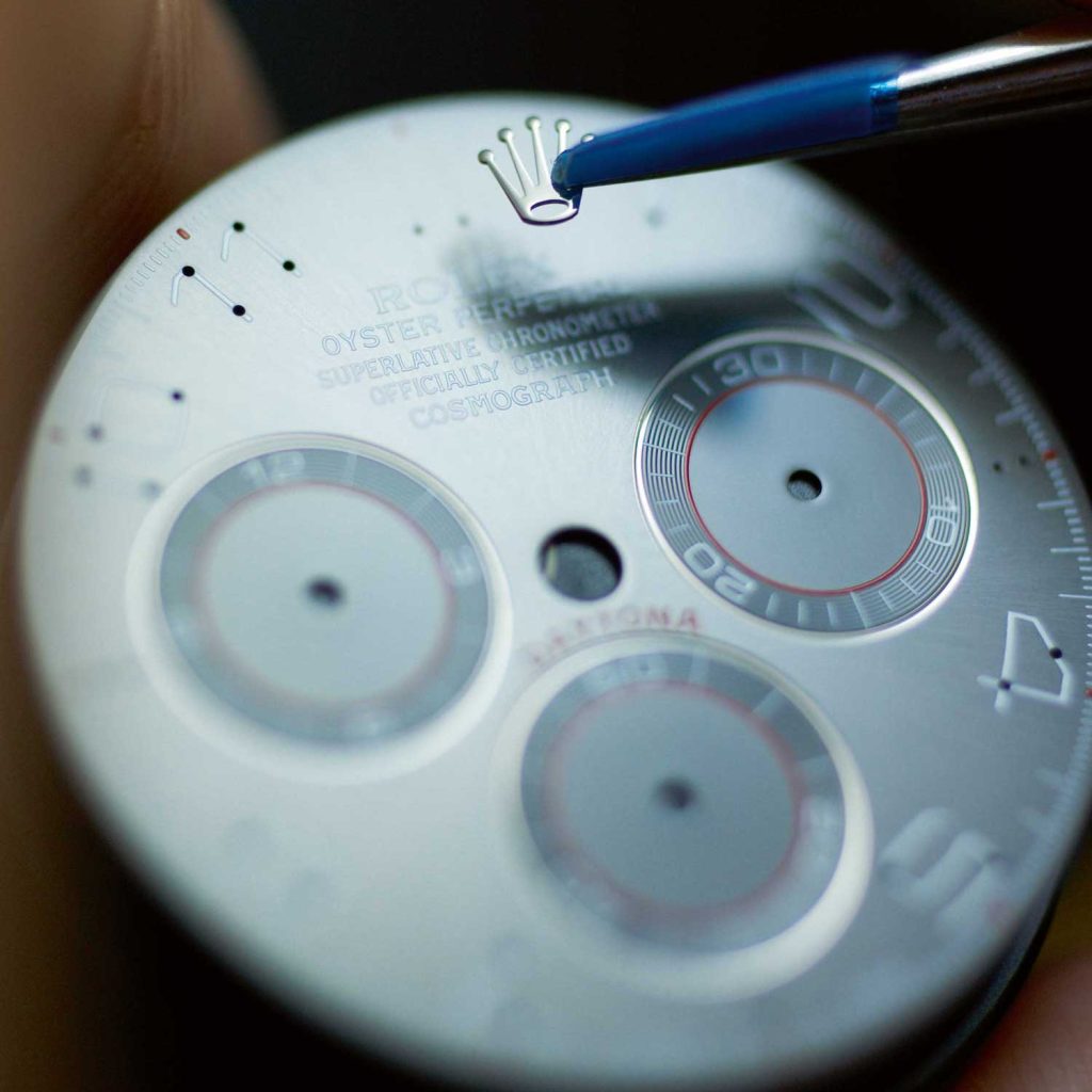 A watchmaker is applying the brand’s logo on a Daytona dial