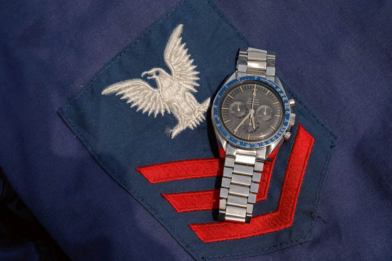Steel Omega Speedmaster ref. 105.012 with cal. 321, 1965. Brownish dial with discoloured blue bezel. Vintage U.S. Navy jacket, 1960