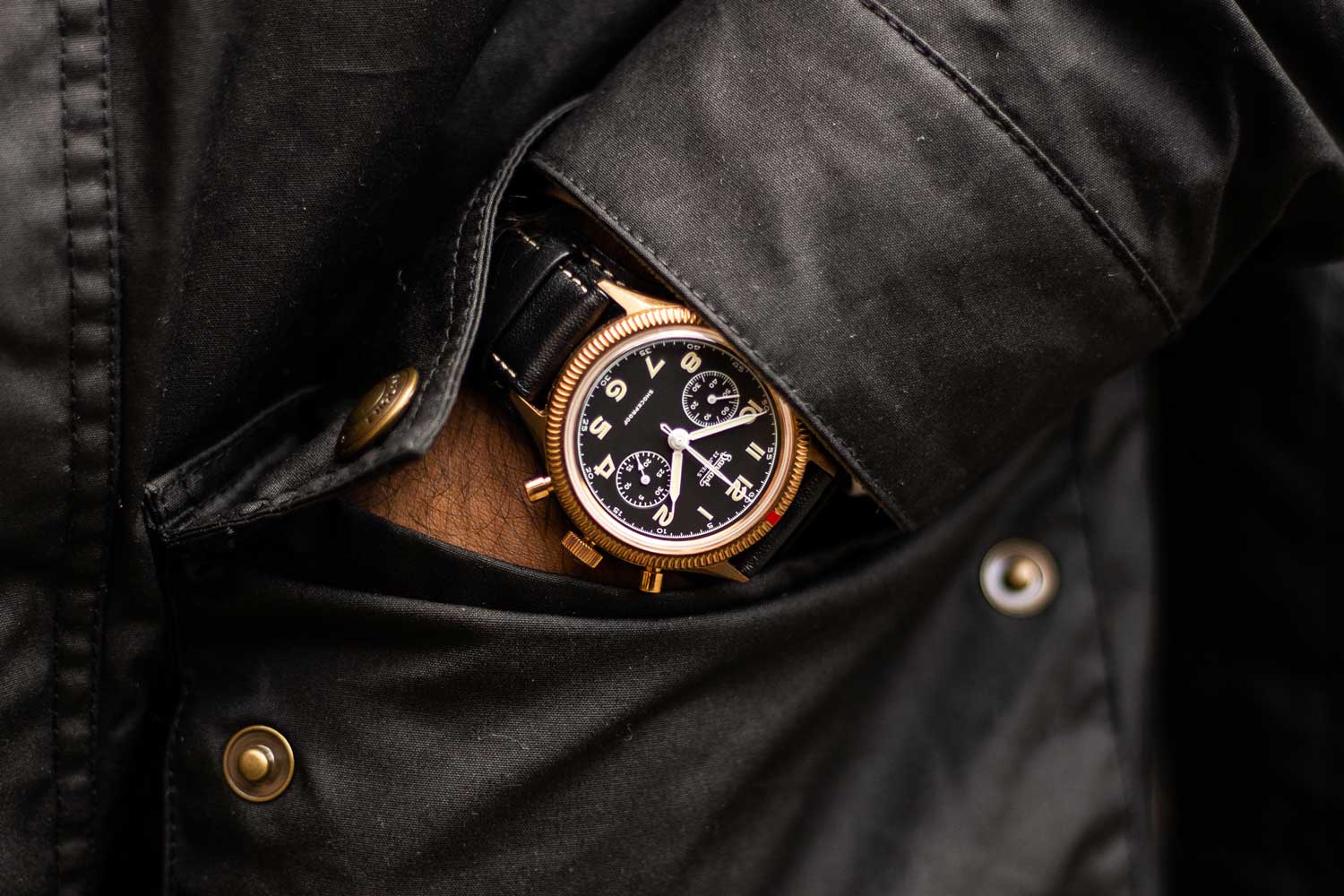 The Hanhart x The Rake & Revolution Limited Edition Bronze 417 Chronograph seen here paired with our exclusive faded vintage black Belstaff jacket completed by its brass snaps and zipper (©Revolution)