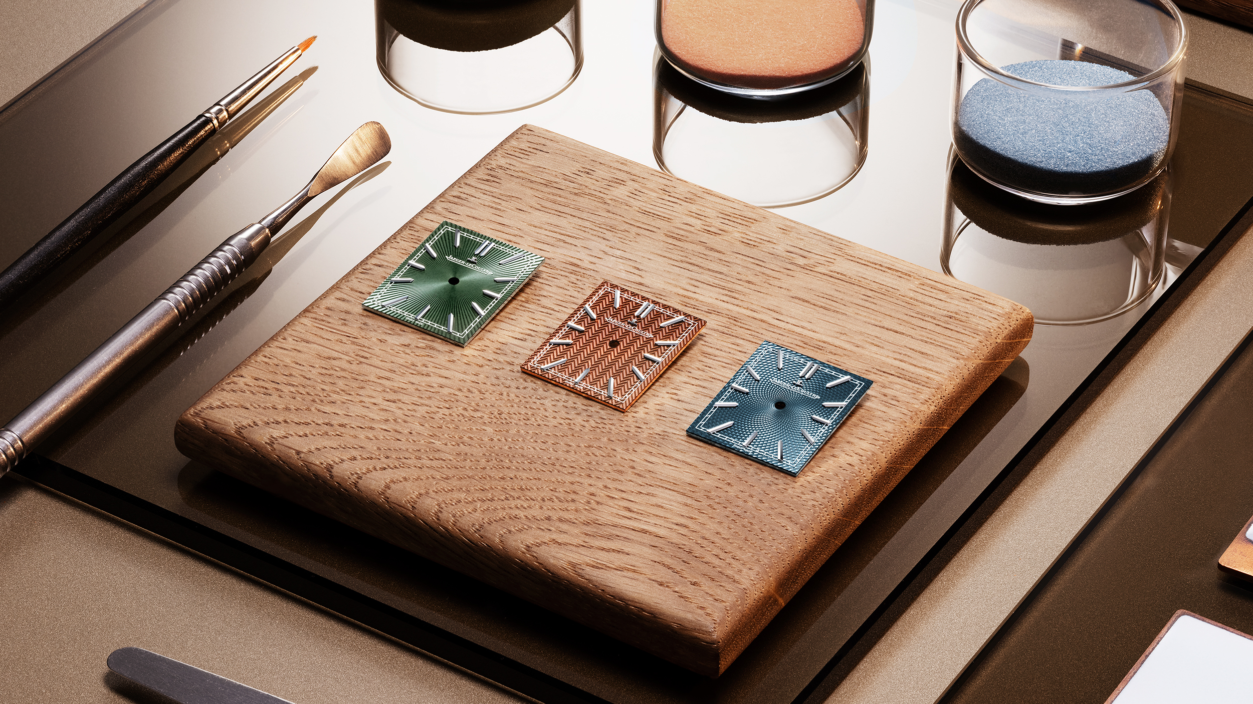 Close-up of three square Reverso dials in green, bronze, and blue, each featuring a distinct guilloché pattern with translucent grand feu enamel