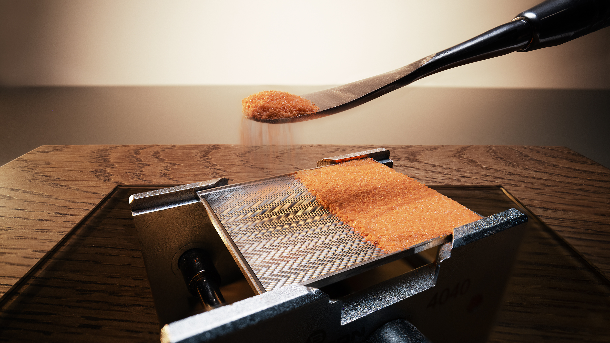 Close-up of orange enamel powder being evenly spread on a herringbone guilloché dial plate during the grand feu enamelling process, before multiple firings in the kiln.