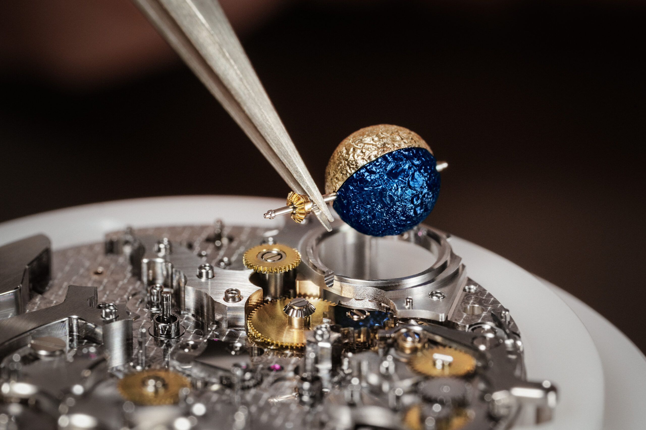 Close-up of spherical moon phase component being assembled into the Calibre 3670, showing gold and blue surface texture.