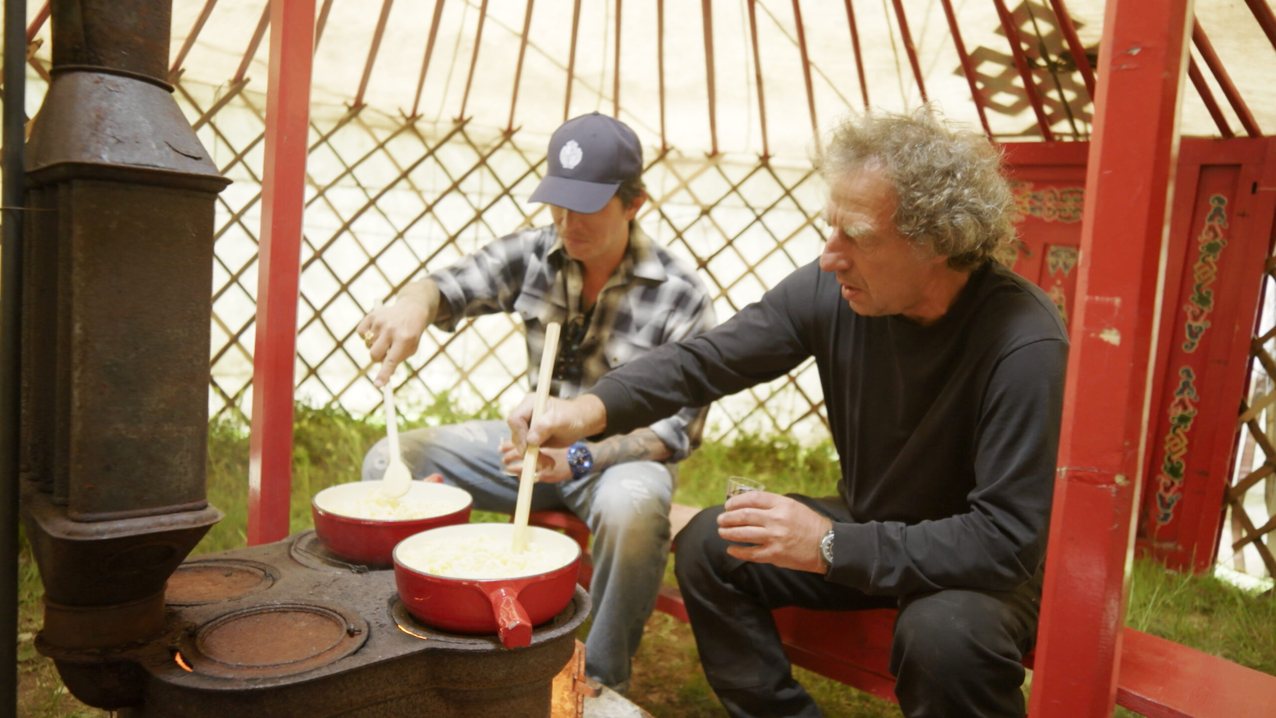 Wei Koh and Denis Flageollet cooking and stirring fondue together inside a red-framed Mongolian yurt for Man of the Hour