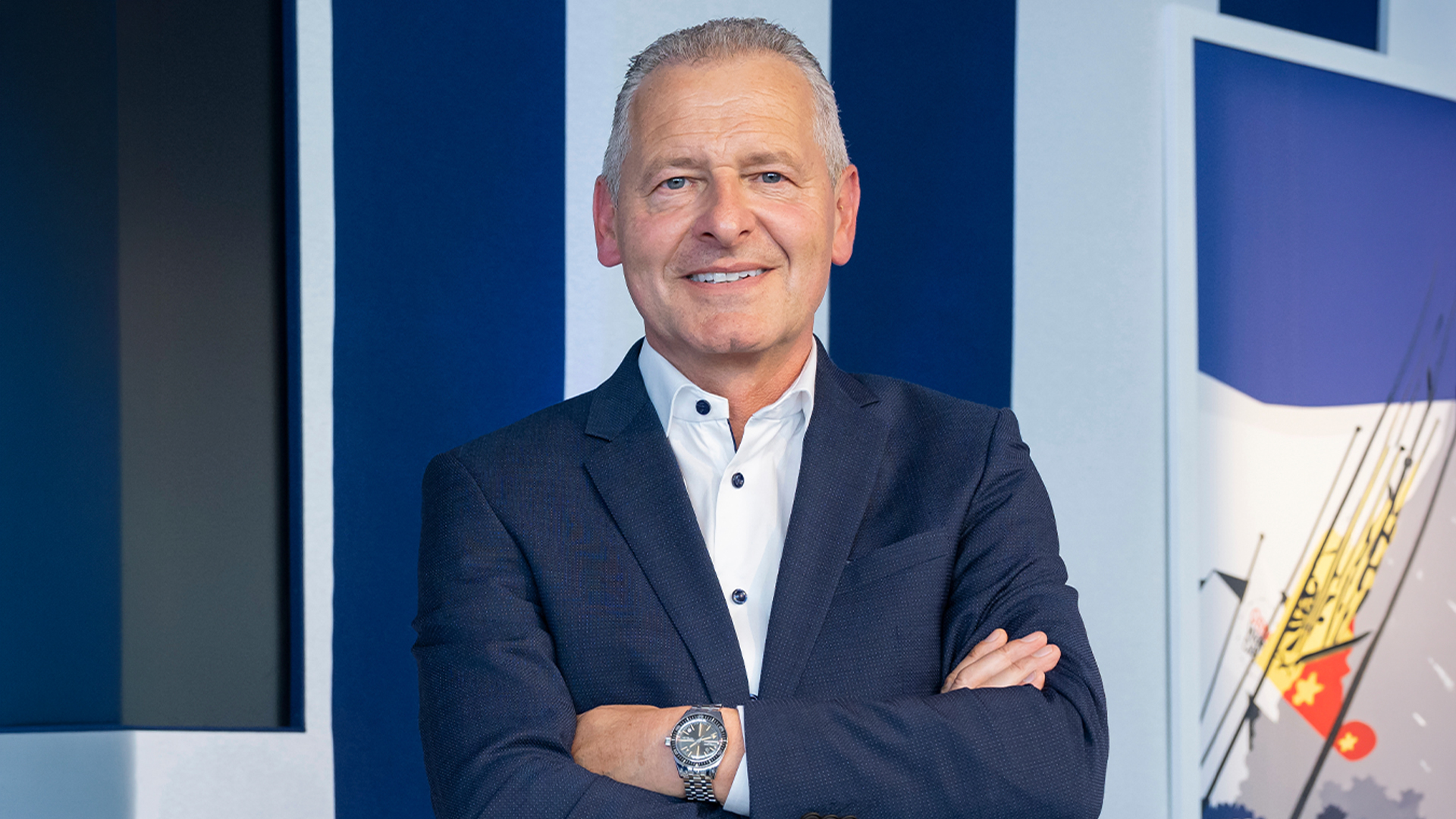 Portrait of Patrik Hoffmann standing with arms crossed, wearing a suit and wristwatch