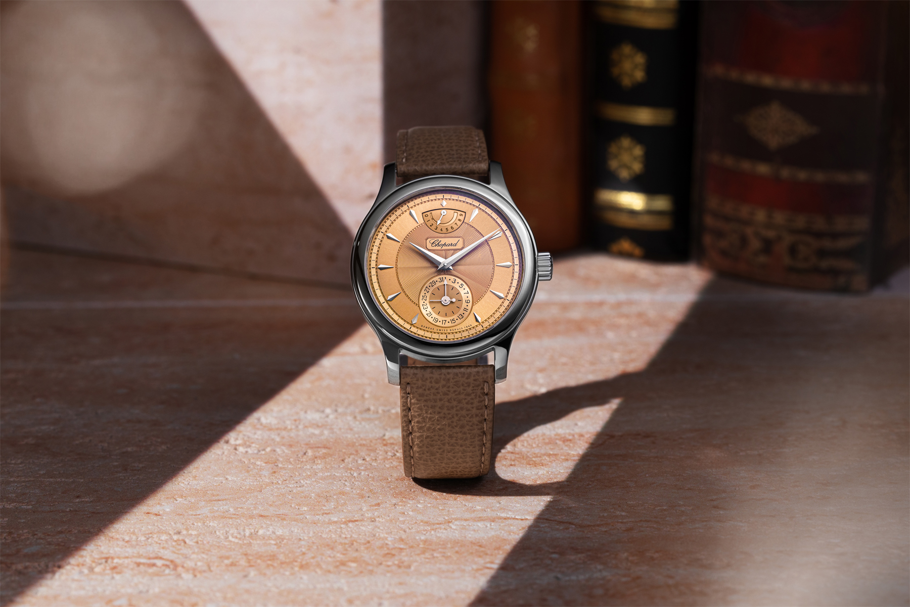 The Chopard L.U.C Quattro Origin floating against a warm abstract background of light and shadow, dial facing forward, tan leather strap visible