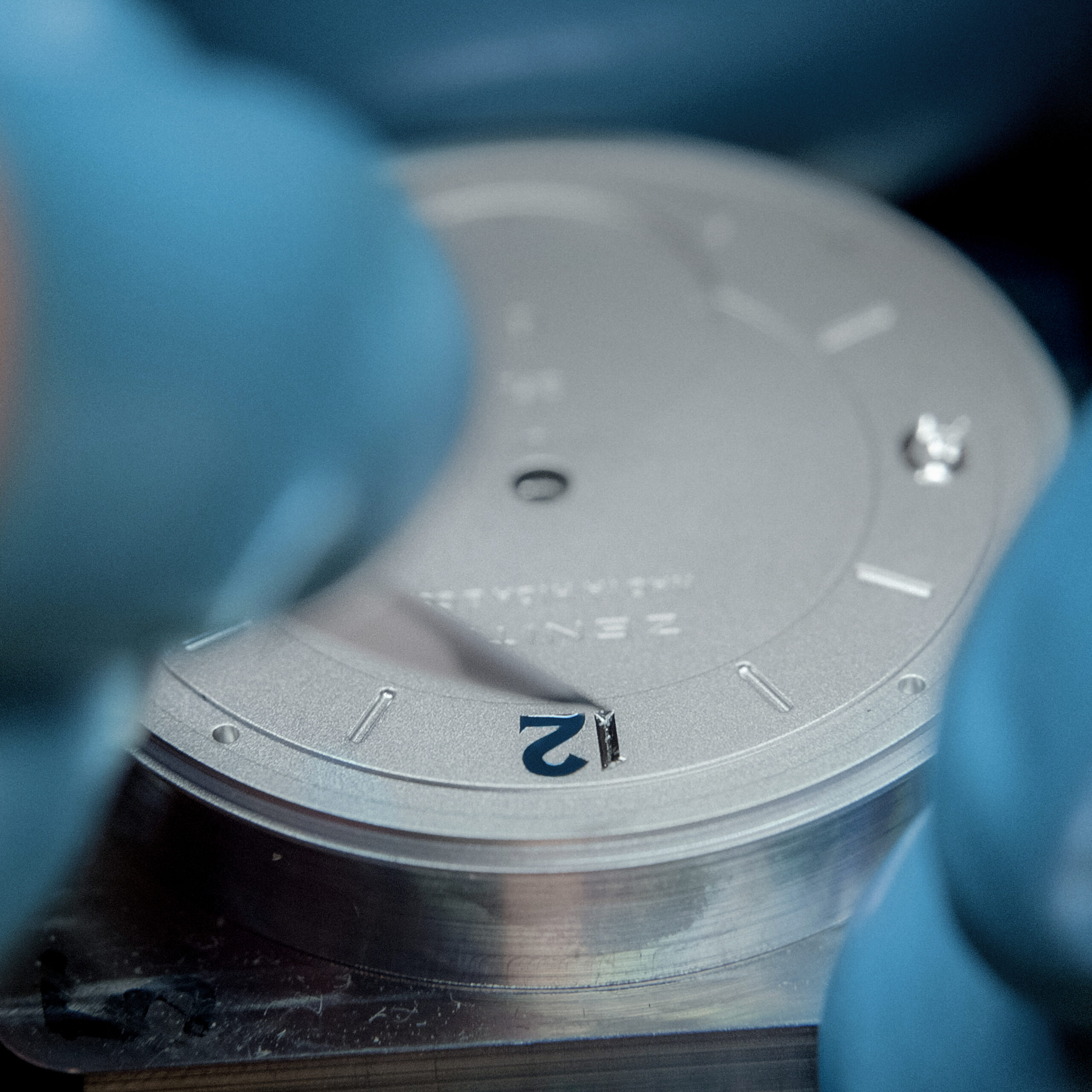 Close-up of blue Japanese urushi lacquer being applied to an engraved numeral on the silver dial of the Zenith G.F.J.