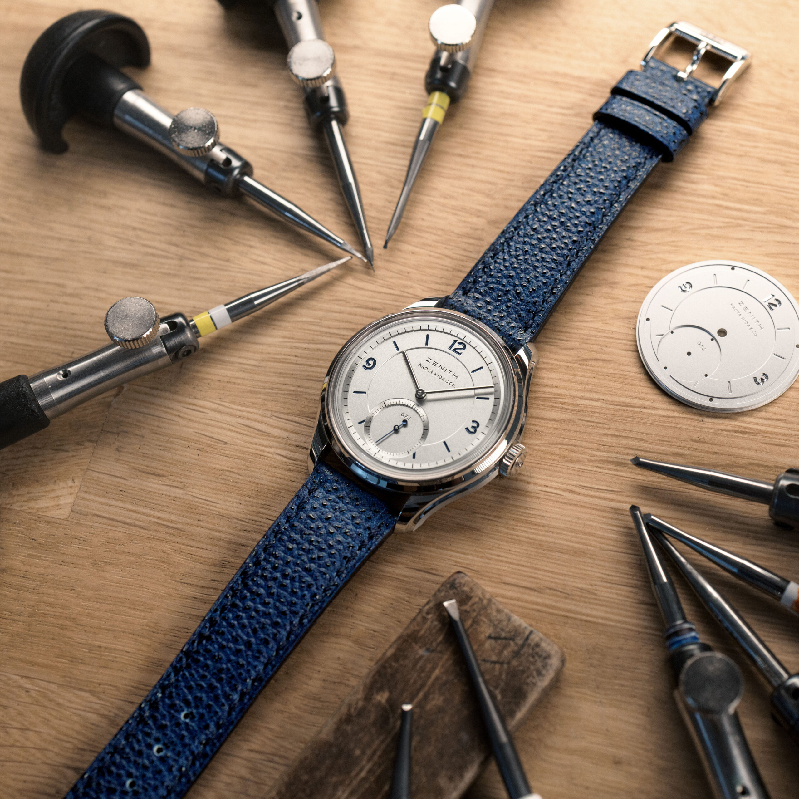 Flatlay of the Zenith G.F.J. Calibre 135 Double Signed with Naoya Hida & Co. surrounded by watchmaking tools on a wooden workbench